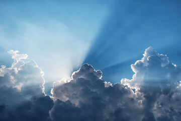 Sunbeams through a dark cumulus cloud in a blue sky