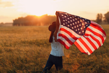 Woman farmer in the agricultural field with american flag on sunset.