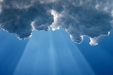 A wide sunbeam on a blue sky under the dark clouds