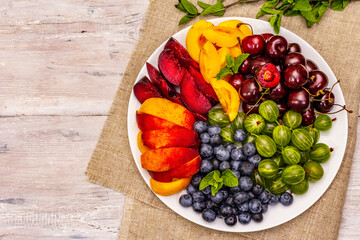 Assorted fresh berries of a cherry, gooseberry, blueberries, slices of ripe peach, plum and...