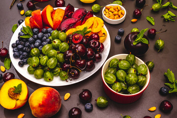Assorted fresh berries of a cherry, gooseberry, blueberries, slices of ripe peach, plum and apricot, fragrant mint on a plate