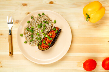 Green buckwheat with baked eggplant with tomato and garlic on a plate with a fork next to vegetables.