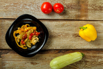 Vegetable stew stew on a black plate and a number of vegetables on a wooden table.