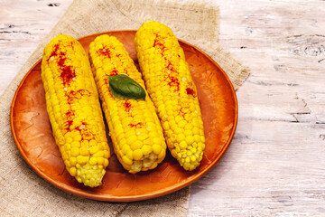 Boiled corn cobs on ceramic plate. Sea salt, fragrance paprika, fresh basil leaf