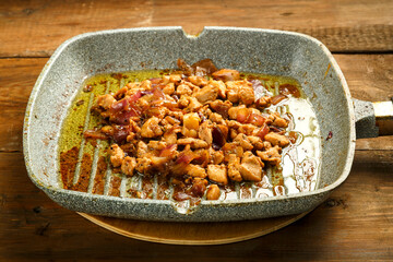 Frying pan with fried chicken fillet and onions on a wooden table.