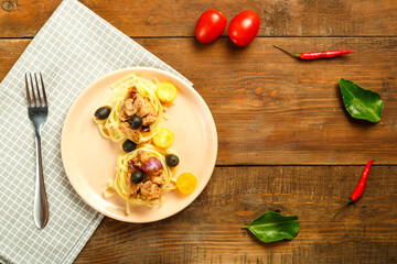 Pink plate with spaghetti nests stuffed with chicken fillet with olives on the table on a napkin next to a fork.