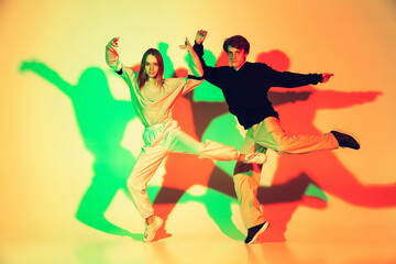Young man and woman, couple dancing hip-hop, street style isolated on studio background in colorful neon light. Fashion and motion, youth, music, action concept. Trendy clothes. Copyspace for ad.