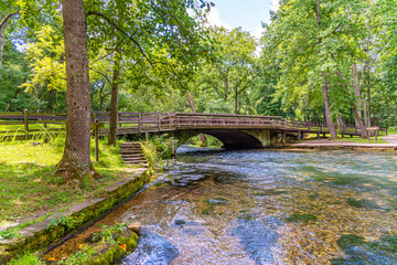 Fototapeta na wymiar Clear water of river flowing under bridge in park in forest