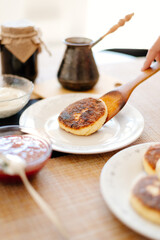 Cheese pancakes on a wooden spatula. Breakfast at home. The housewife puts the cheesecake on the plate.
