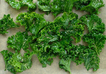 Sliced fresh curly kale with salt, pepper and sesame seeds on brown baking paper.