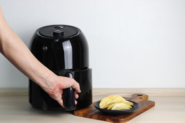 a black air fryer or oil free fryer appliance is on the wooden table in the kitchen with deep fried potato chips in black dish on the wooden tray