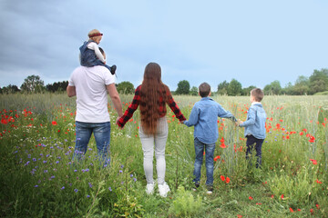 blooming red poppies in a green summer field, a man holding a daughter, wife, two sons on his neck, the concept of a happy relationship, love and family happiness