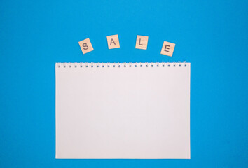 On a blue background is an inscription in wooden letters sale, with a vertically Notepad under the copy space. the concept of school sales