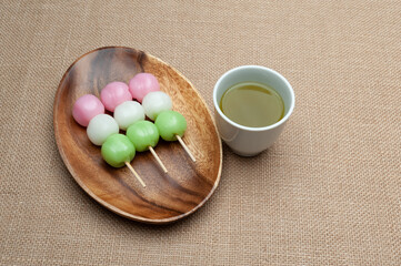 Japanese traditional sweet called Dango Mochi on wooden platter with green tea. Isolated on jute background. Close-up. Top view. Copy space.