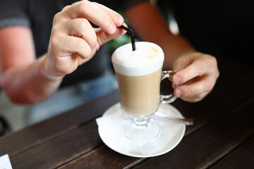 Man's hand holds glass with a latte and straw. Types of coffee drinks concept