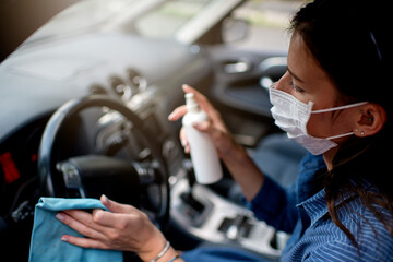 Woman with protective face mask cleaning car interior to prevent virus spread 