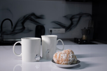 two white cups with tea and sticking out tea bags next to gingerbread cookies heart-shaped on a white table in a gray kitchen. High quality photo