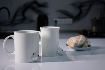 two white cups with tea and sticking out tea bags next to gingerbread cookies heart-shaped on a white table in a gray kitchen. High quality photo