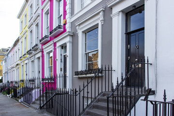 Fototapeta na wymiar Row of colorful typical houses and stairs in Notting Hill, London, UK. Colorful English houses facades in blue, pink, yellow and white colors. British pastel buildings. Real estate concept urban scene