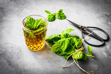 Pfefferminztee in einem Glas, ein Bund frische Minze und eine Gartenschere auf einem grauen...