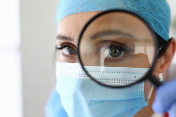 Doctor woman with medical mask looks through magnifying glass. Medical research disease concept