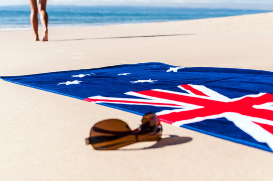 Woman walking away from Australian flag towel and sunglasses towards the ocean to swim. - Powered by Adobe