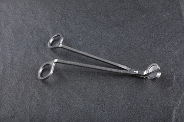 a silver aluminium wick trimmer for candle is put on the grey stone floor