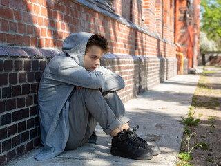 A lonely, sad teenager sits alone on the street near the house. quarrel with parents, problems at school. problems and psychology of adolescents, concept