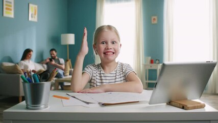 Funny girl portrait sitting at work desk at home, looking at camera and makes funny faces, in wireless headset, raising hand, has fun, parents are on the background, Slow motion.
