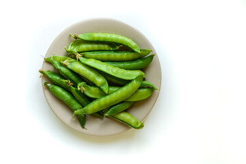 A pile of raw green peas in brown plate, fresh harvest from garden. Healthy vegetarian food concept, isolated on white background