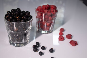transparent glasses with currants and raspberries on a white table in a gray kitchen. High quality photo