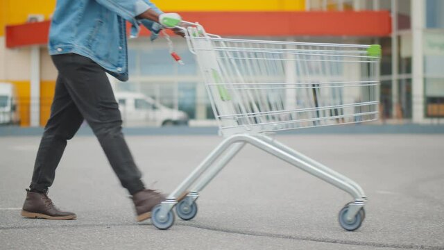Side view of african man with shopping cart walking in parking lot