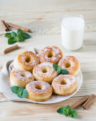 Homemade ring-shaped sugared donuts on a white plate on a light wooden background, rustic style