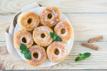 Homemade ring-shaped sugared donuts on a white plate on a light wooden background, rustic style