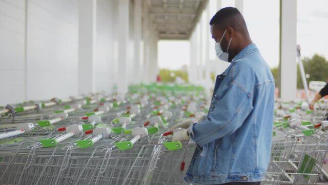 African man wearing protective facial mask and gloves pulling empty shopping cart