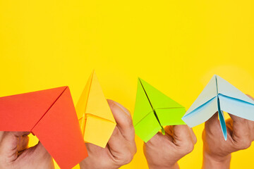 Hands throw paper planes multicolored on yellow background copy space