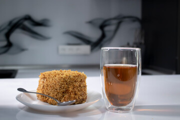 cup of tea in a double-botoom glass and piece of cake on white table in gray kitchen. High quality photo