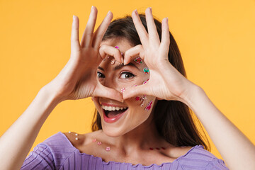 Image of young joyful woman with stickers on face showing heart gesture