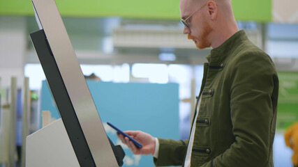 Side view of young man paying at self-checkout using smartphone app at store