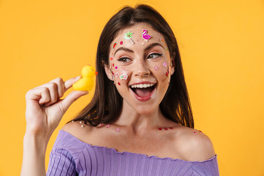 Image of young joyful woman with stickers on face holding rubber duck