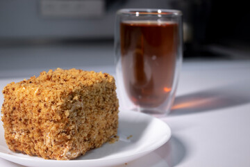 cup of tea in a double-botoom glass and piece of cake on white table in gray kitchen. High quality photo