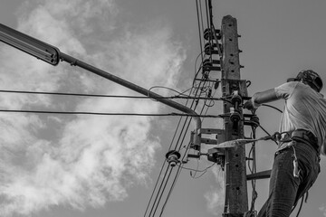 Electricians working on power pole connecting cables with clear sky background.- Concept of...