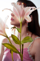 Blonde girl wearing makeup behind beautiful pink lilies in studio