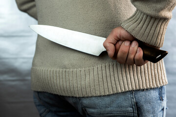 An evil man holds a knife behind his back, waiting for the victim. A maniac and a rapist with a gun.