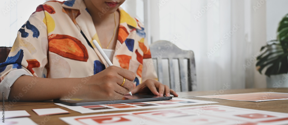 Poster a graphic developer is using a computer tablet and stylus pen at the wooden working desk.