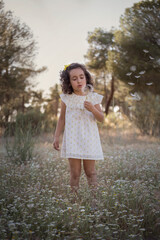 Little girl in the field on a summer afternoon blowing a dandelion flying through the air. Curly black hair.