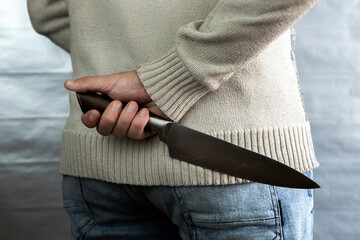 An evil man holds a knife behind his back, waiting for the victim. A maniac and a rapist with a gun.