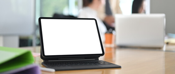 Blank screen computer tablet is putting on the wooden table over the meeting room as a background.