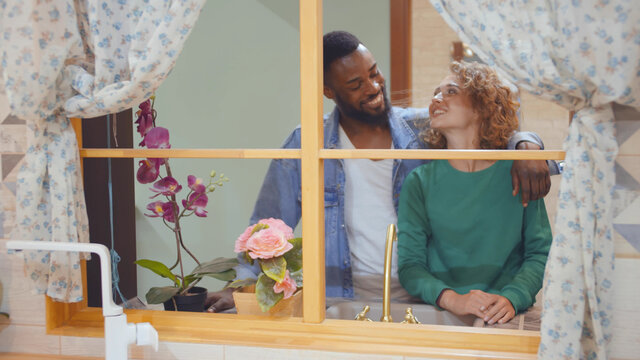 Portrait of happy diverse couple looking out of artificial window shopping in kitchen interior store