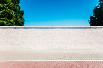 An urban minimalist scene, a white wall in the sun with two trees and blue sky.